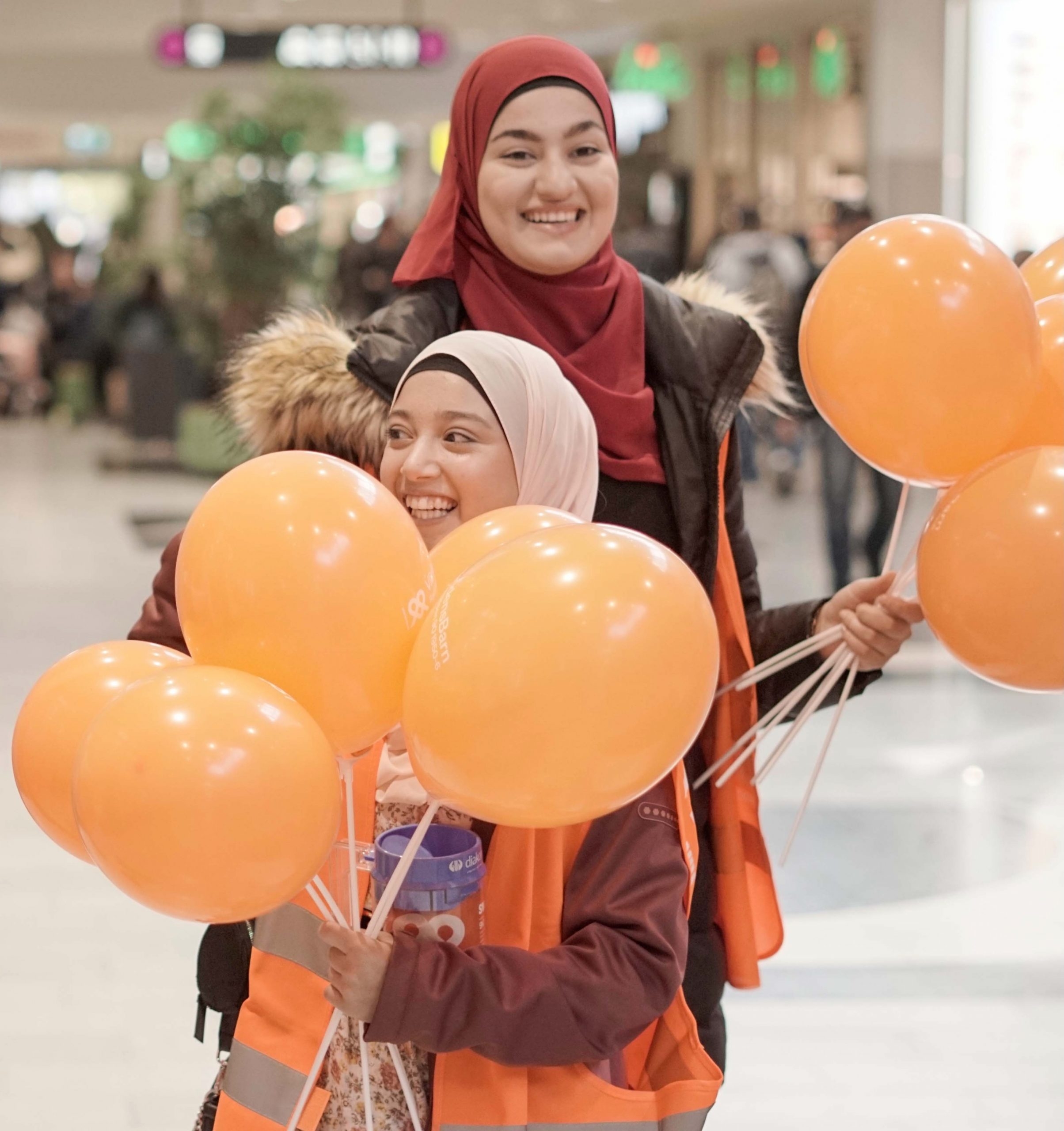 Två tjejer med slöja skrattar och håller i ballonger.